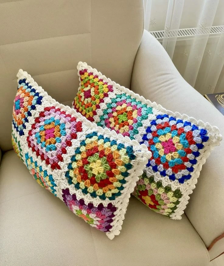 Almofadas coloridas feitas à mão com crochê em padrões geométricos, mostrando detalhes dos pontos e cores vibrantes.