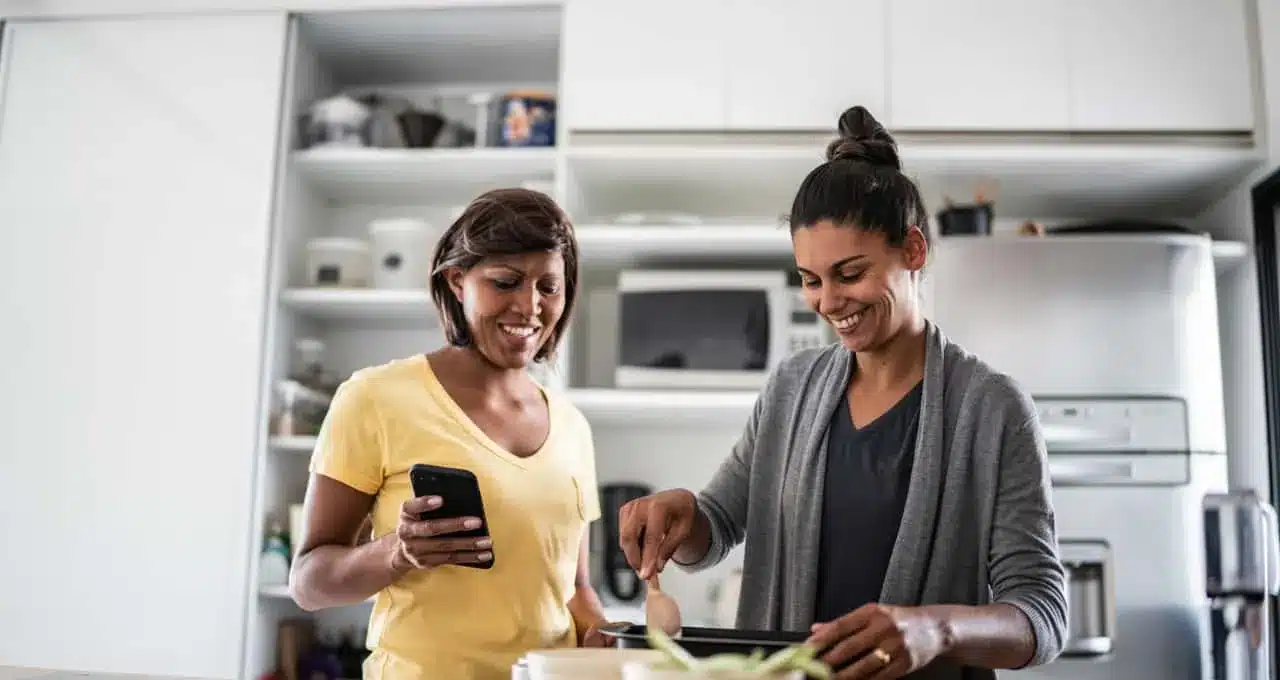 Duas mulheres cozinhando juntas enquanto usam o celular para consultar receita