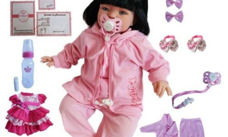 Boneca bebê reborn realista vestida de rosa com acessórios infantis ao redor
