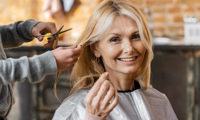 Mulher madura sorrindo enquanto recebe um corte de cabelo moderno em salĂŁo, valorizando a beleza natural aos 70 anos.