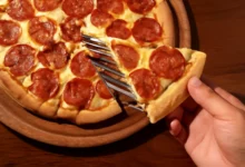 Pizza de pepperoni caseira sendo servida, com queijo derretido e crosta dourada.