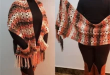 Cachecol de crochê em tons terrosos com franjas, usado sobre roupa preta.
