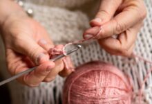 Mãos femininas fazendo crochê com fio rosa, representando o processo artesanal de criação de peças para cozinha