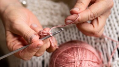 Mãos femininas fazendo crochê com fio rosa, representando o processo artesanal de criação de peças para cozinha
