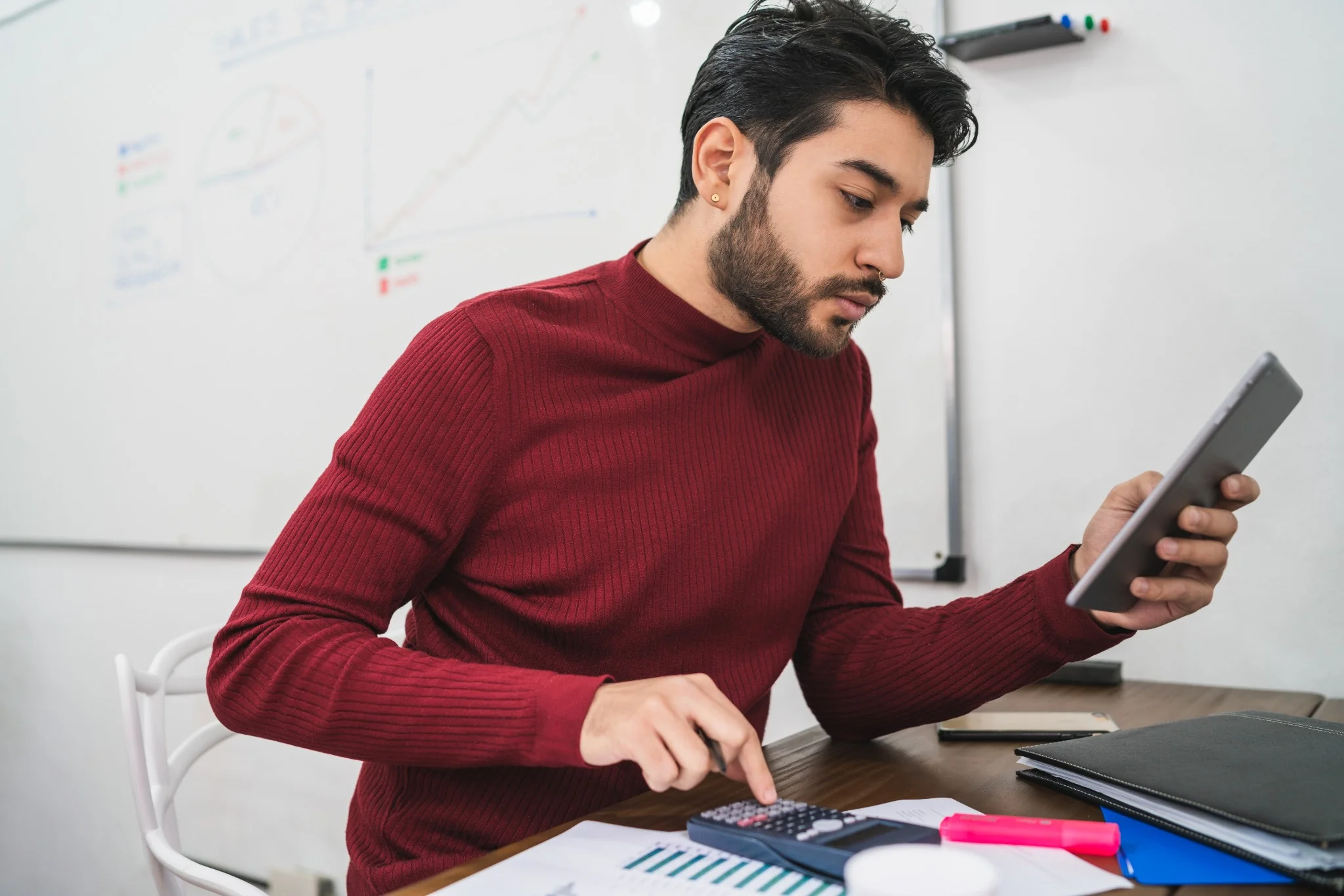 Profissional usando calculadora e tablet, representando o trabalho de contabilidade especializada.