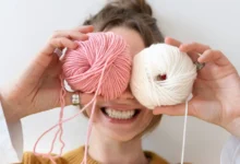 Mulher sorridente segurando novelos de lã rosa e creme, simbolizando a criatividade do crochê no dia a dia.