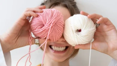 Mulher sorridente segurando novelos de lã rosa e creme, simbolizando a criatividade do crochê no dia a dia.