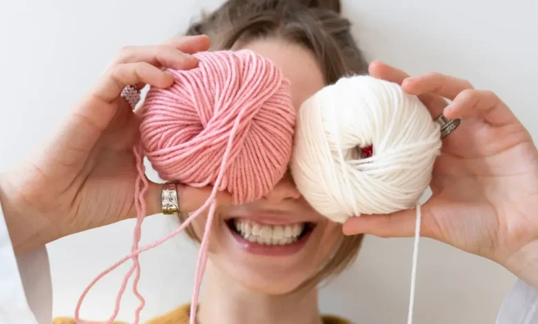 Mulher sorridente segurando novelos de lĂŁ rosa e creme, simbolizando a criatividade do crochĂȘ no dia a dia.