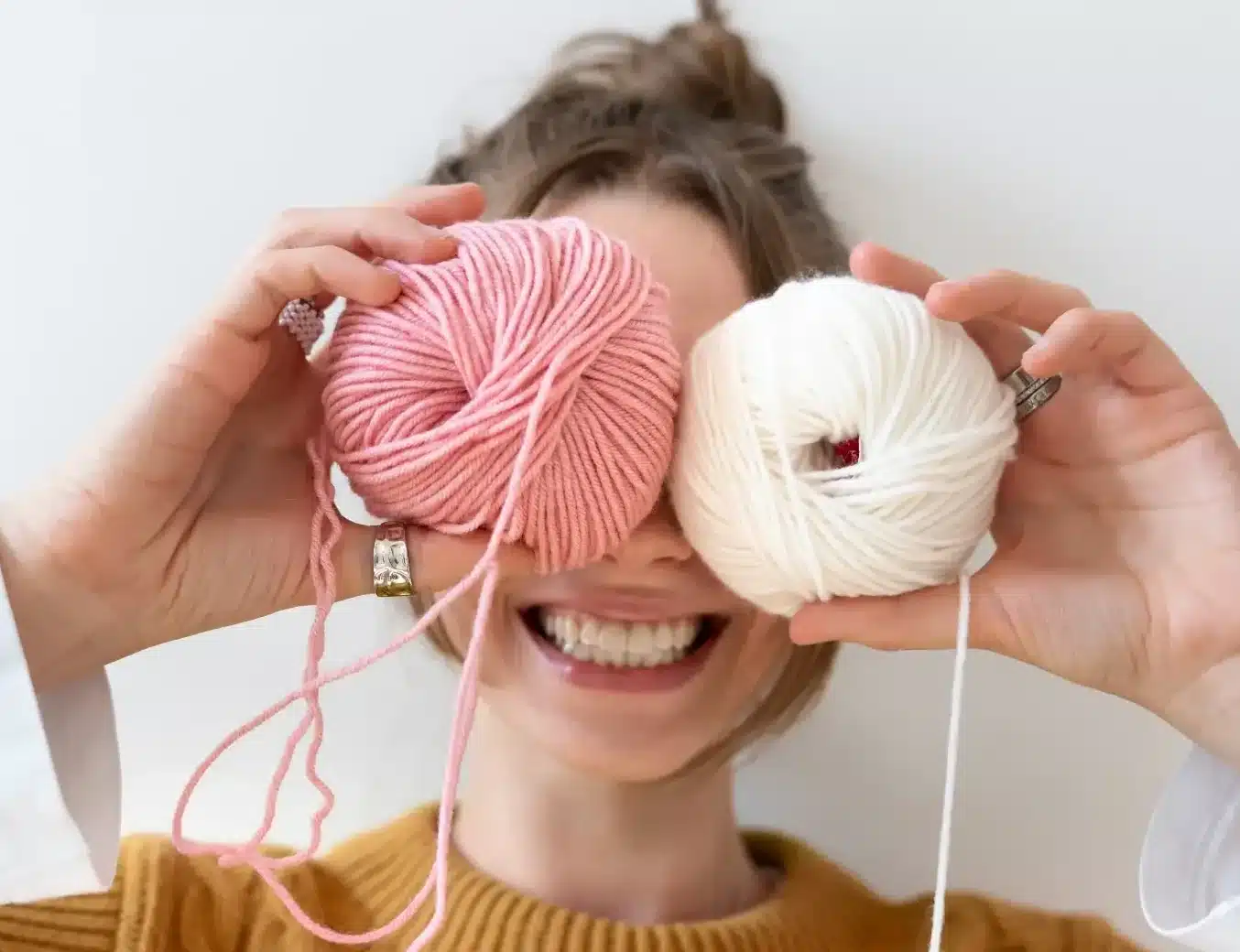 Mulher sorridente segurando novelos de lã rosa e creme, simbolizando a criatividade do crochê no dia a dia.