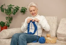 Mulher idosa praticando crochê com linha azul, criando uma obra de arte têxtil.