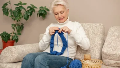 Mulher idosa praticando crochê com linha azul, criando uma obra de arte têxtil.