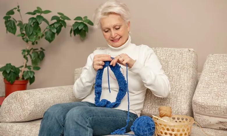 Mulher idosa praticando crochĂȘ com linha azul, criando uma obra de arte tĂȘxtil.
