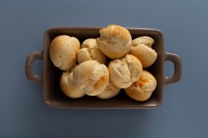 Pães delícia dispostos em travessa marrom sobre fundo azul, vistos de cima.