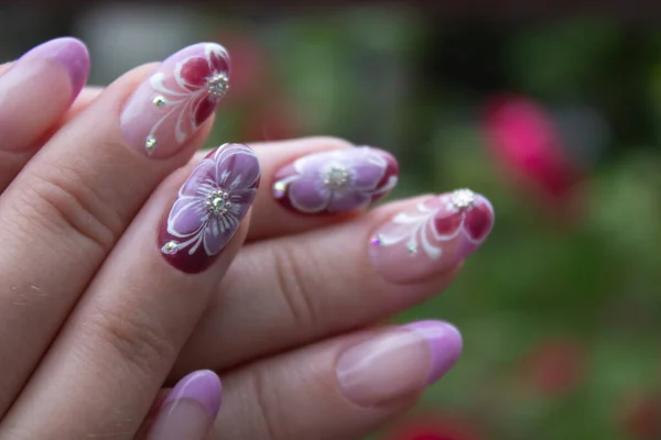 Unhas decoradas com flores roxas e pedrarias, tendência para mulheres maduras