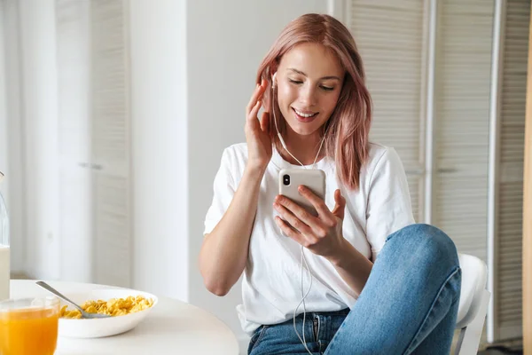 Mulher sorrindo enquanto ouve música no celular durante o café da manhã