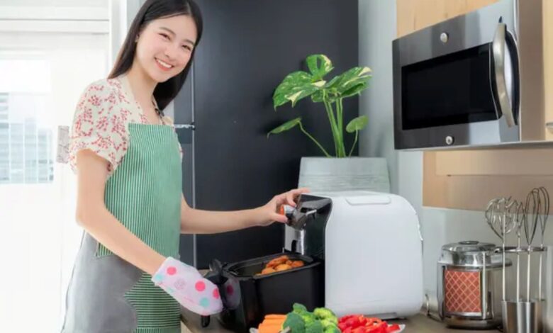 Mulher cozinhando legumes e batatas na air fryer em uma cozinha moderna