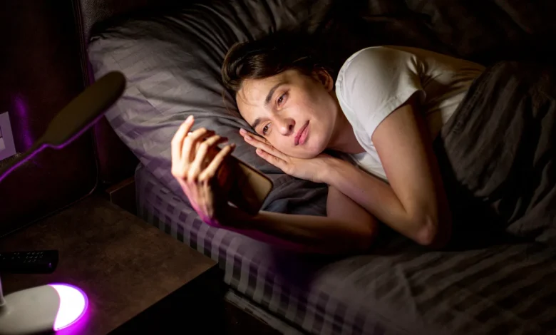 Pessoa sorridente deitada na cama, olhando para o celular à noite, transmitindo uma mensagem de boa noite cheia de carinho e aconchego