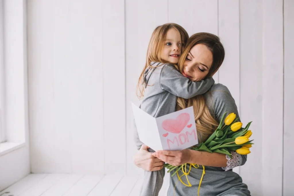 Mãe e filha compartilhando um abraço afetuoso enquanto a filha segura um cartão de Dia das Mães com um desenho de coração