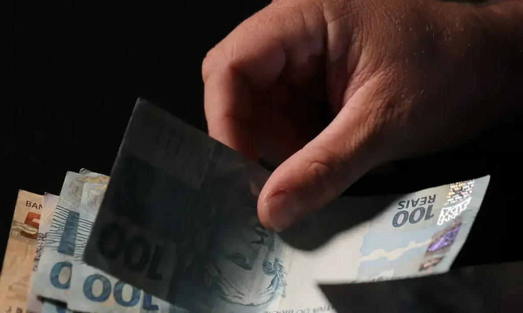 Pessoa segurando cédulas de reais, representando dinheiro em mãos