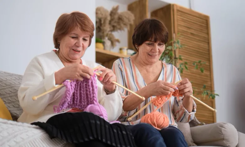 Duas mulheres idosas sorrindo enquanto fazem crochĂȘ com fios coloridos, demonstrando habilidade e concentração