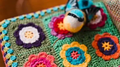 Peça de crochê colorida com flores e pássaro decorativo, mostrando uma embalagem criativa e artesanal para vendas.