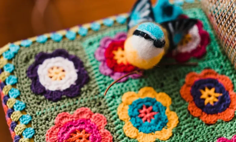 Peça de crochê colorida com flores e pássaro decorativo, mostrando uma embalagem criativa e artesanal para vendas.