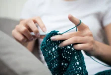 Mãos segurando agulha de crochê e fio azul, fazendo pontos em crochê