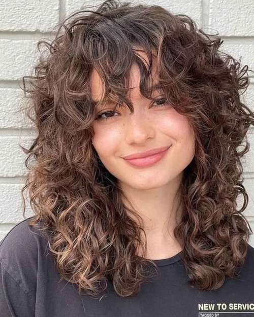 Mulher com cabelo cacheado em corte butterfly cut, realçando o volume natural dos fios