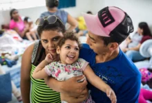 Criança sorridente com deficiência causada pelo vírus Zika sendo abraçada por adultos em ambiente comunitário.