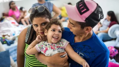 Criança sorridente com deficiência causada pelo vírus Zika sendo abraçada por adultos em ambiente comunitário.