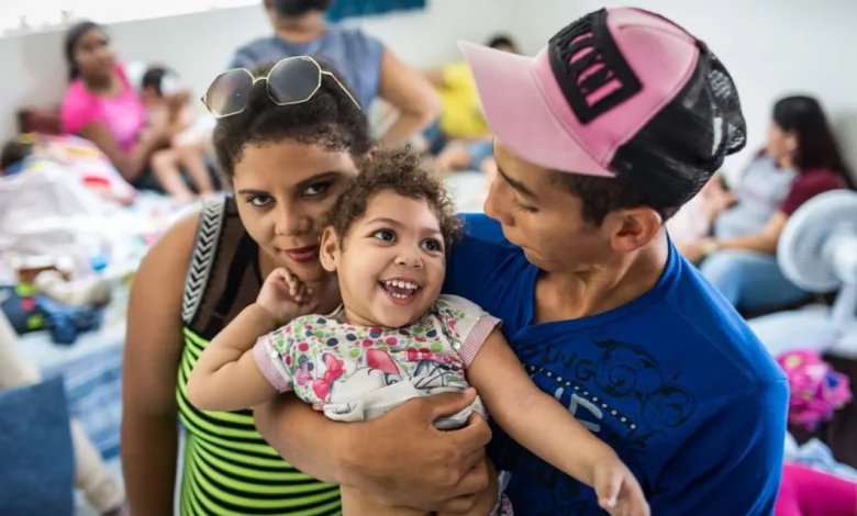 Criança sorridente com deficiência causada pelo vírus Zika sendo abraçada por adultos em ambiente comunitário.