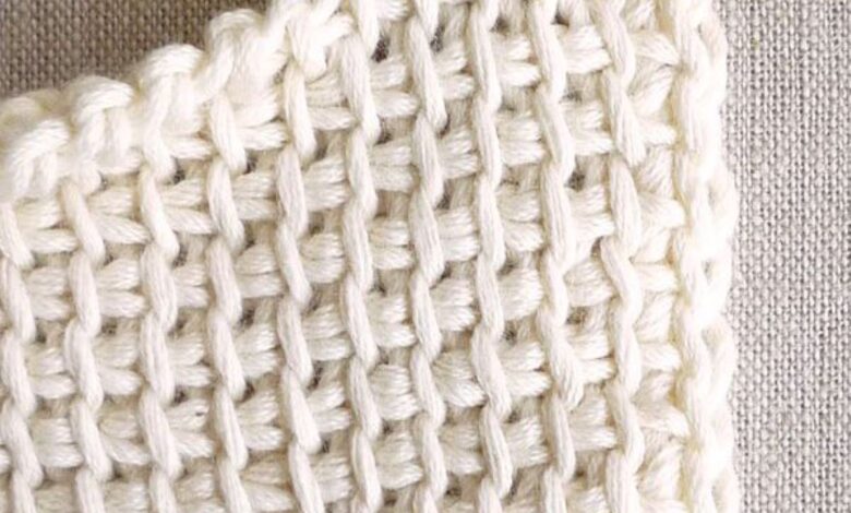 Detalhe de ponto de crochê branco feito à mão com agulha de crochê vermelha.