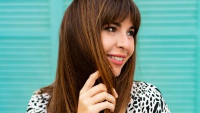 Mulher sorrindo com cabelo castanho médio, liso e franja reta estilizada