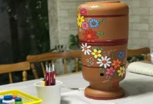 Filtro de barro decorado com flores, sobre mesa com pincéis e tintas
