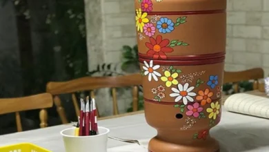 Filtro de barro decorado com flores, sobre mesa com pincéis e tintas