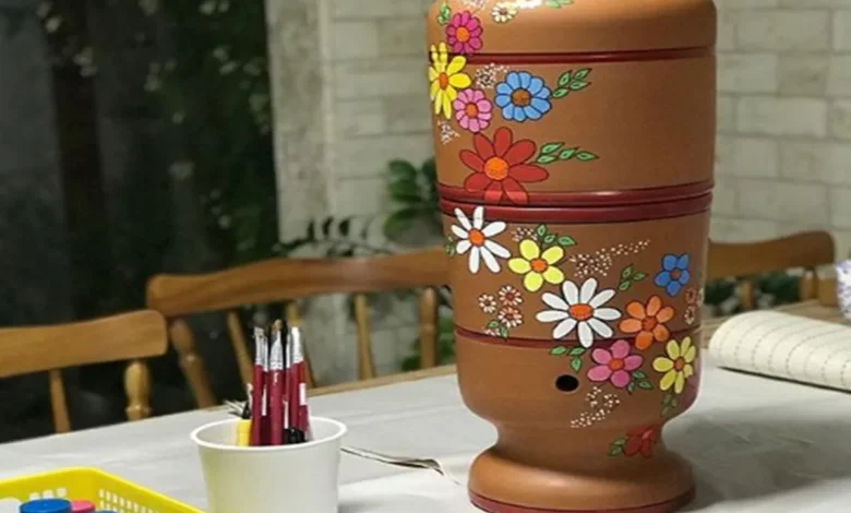 Filtro de barro decorado com flores, sobre mesa com pincéis e tintas