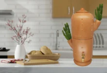 Filtro de barro com formato criativo de cacto, com detalhes de plantas no topo, exibido em uma bancada de cozinha moderna