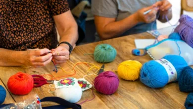 Duas pessoas praticando crochê com fios coloridos sobre uma mesa de madeira