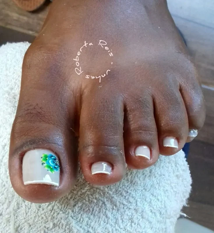 Unhas dos pés com francesinha branca e detalhe de flor azul decorativa no dedão