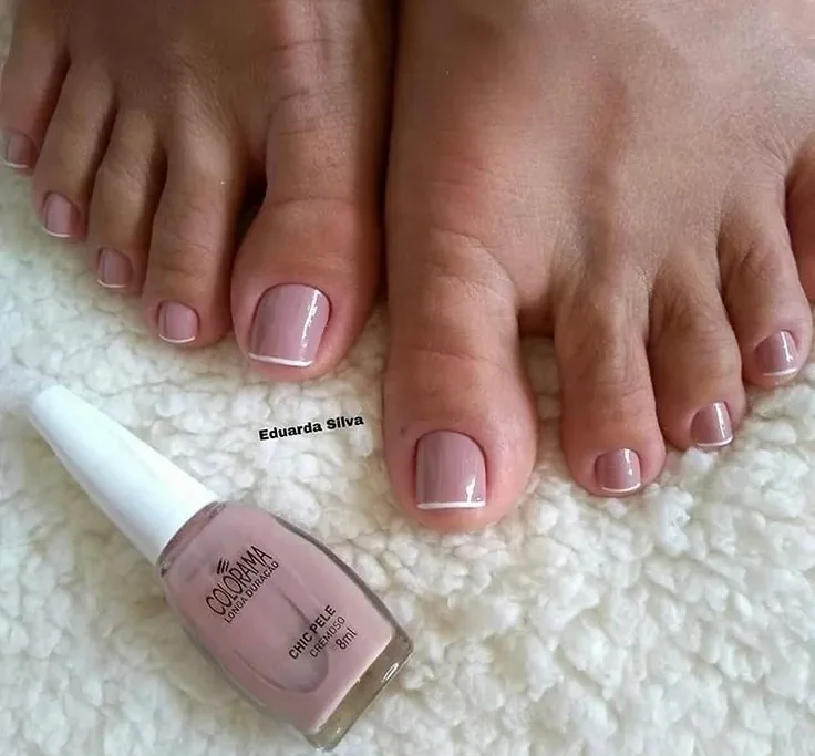 Unhas dos pés com esmalte nude e francesinha branca, ao lado de frasco de esmalte