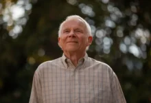 Homem idoso sorrindo, olhando para cima, em ambiente ao ar livre com luz suave