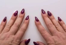 Imagem de mãos femininas com unhas alongadas e decoradas, mostrando as unhas em gel de cor roxa.