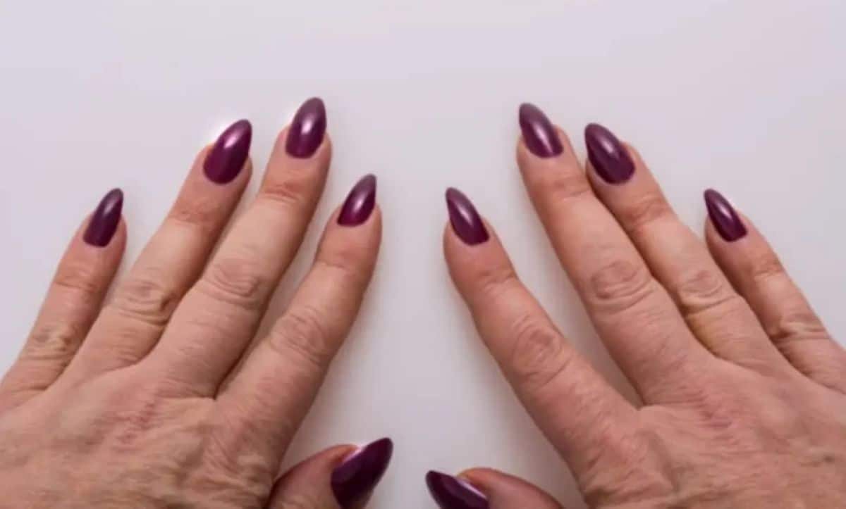 Imagem de mãos femininas com unhas alongadas e decoradas, mostrando as unhas em gel de cor roxa.