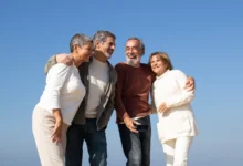 Dois casais idosos felizes aproveitando um dia ao ar livre sob céu azul, sorrindo e se abraçando.