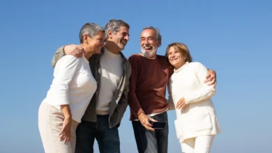 Dois casais idosos felizes aproveitando um dia ao ar livre sob céu azul, sorrindo e se abraçando.