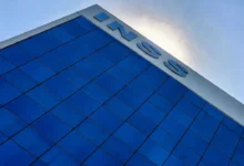 Prédio do INSS com fachada azul refletindo o céu.