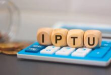 Cubos de madeira formando a palavra IPTU sobre uma calculadora azul, simbolizando o cálculo do imposto