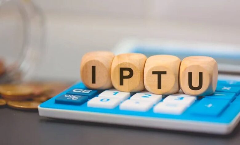 Cubos de madeira formando a palavra IPTU sobre uma calculadora azul, simbolizando o cálculo do imposto