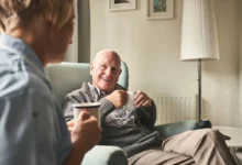 Idoso sorrindo enquanto toma café com cuidador em ambiente acolhedor