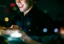 Jovem adulto sorrindo enquanto usa smartphone à noite em ambiente urbano